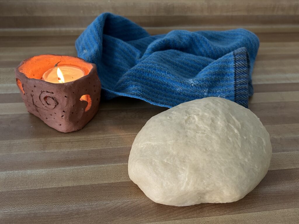 Ball of bread dough sitting on kitchen counter with candle and dishtowel